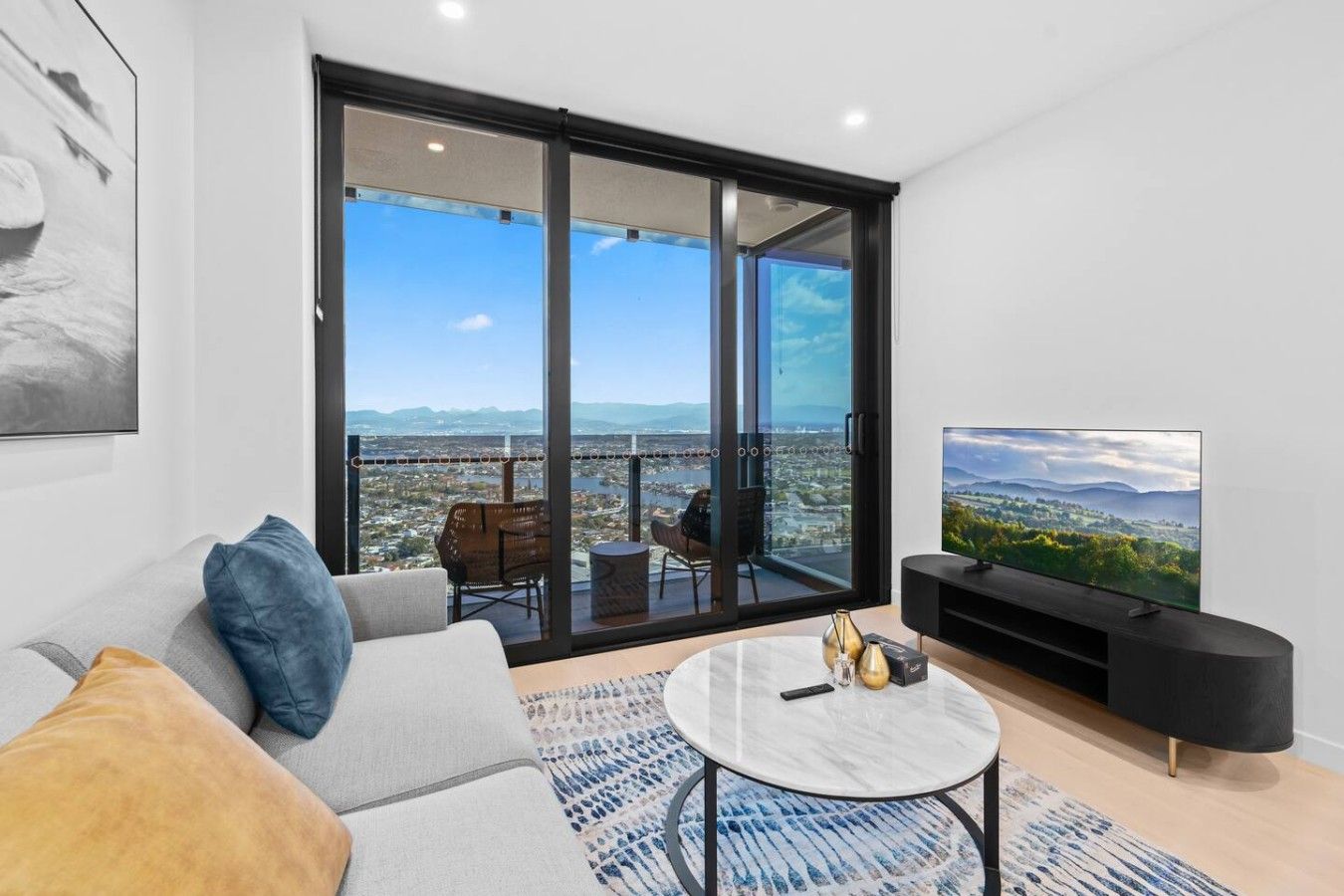 A modern living room with a sofa, a coffee table, a TV, and a balcony with a city view.