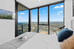Quarto com uma cama grande, vista da cidade através de janelas do chão ao teto e parede de vidro com vista urbana.