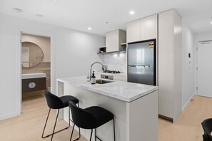A modern kitchen with a central island, stainless steel appliances, and black bar stools. - Stylish 1BR in the Heart of Broadbeach (Broadbeach)