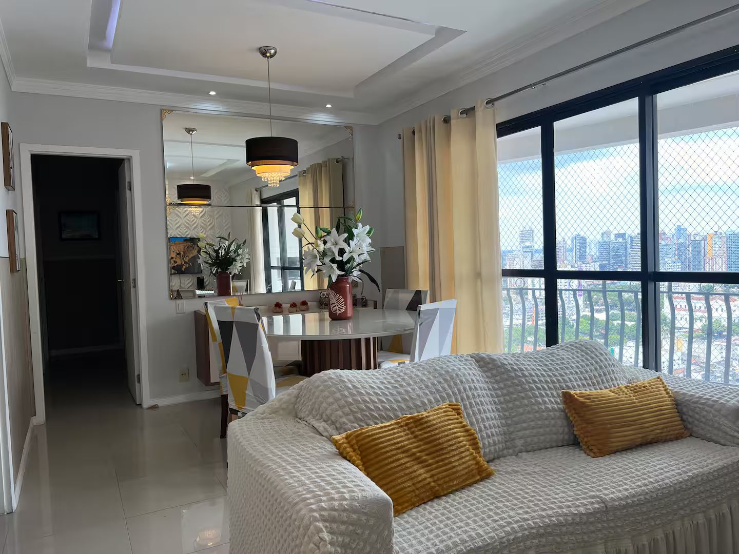 A modern living room with a large window, a dining area, and a view of the cityscape.