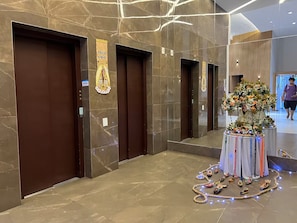 A hotel lobby with marble flooring, a floral centerpiece, and elevator doors with a sign. - 2802 Parc · Luxury and comfortable 3-bedroom apartment with garage (Belém)
