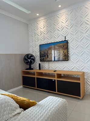 Ein modernes Wohnzimmer mit einem Flachbildfernseher an einer strukturierten Wand, einer Holz-Unterhaltungseinheit mit integrierten Lautsprechern und einem Bett mit einer weißen und gelben Decke.