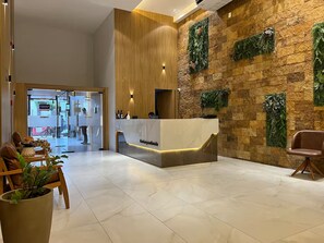 A reception area with a wooden reception desk, a stone wall with greenery, and a potted plant. - 2802 Parc · Luxury and comfortable 3-bedroom apartment with garage (Belém)