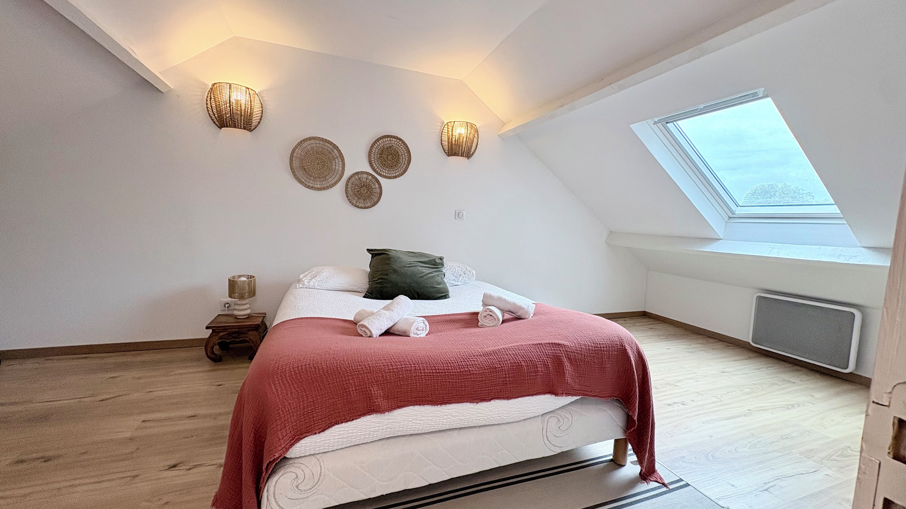 Een slaapkamer met dakraam, een bed met opgerolde handdoeken en wandlampen.