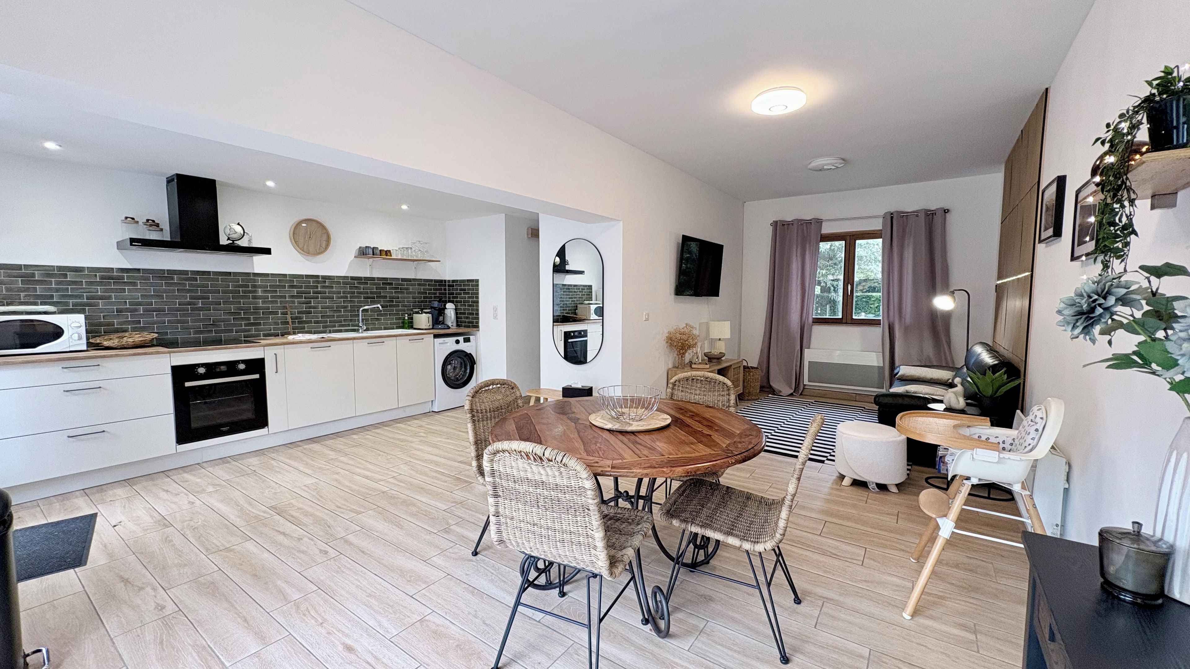 Una cocina moderna con armarios blancos, un microondas y una lavadora. Hay un comedor con una mesa de madera y sillas de mimbre.