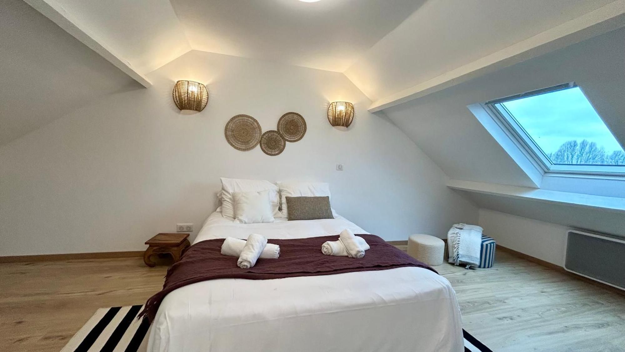 A bedroom with a large bed, a skylight, and wall-mounted lighting fixtures.