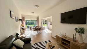 A modern living room with a black leather sofa, a wooden coffee table, and a flat-screen TV mounted on the wall. - 2-bedroom apartment in Ponthoile (Ponthoile)