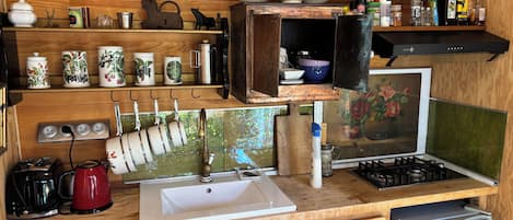 A compact kitchen with wooden cabinetry, a sink, a stove, and various kitchen utensils and appliances.