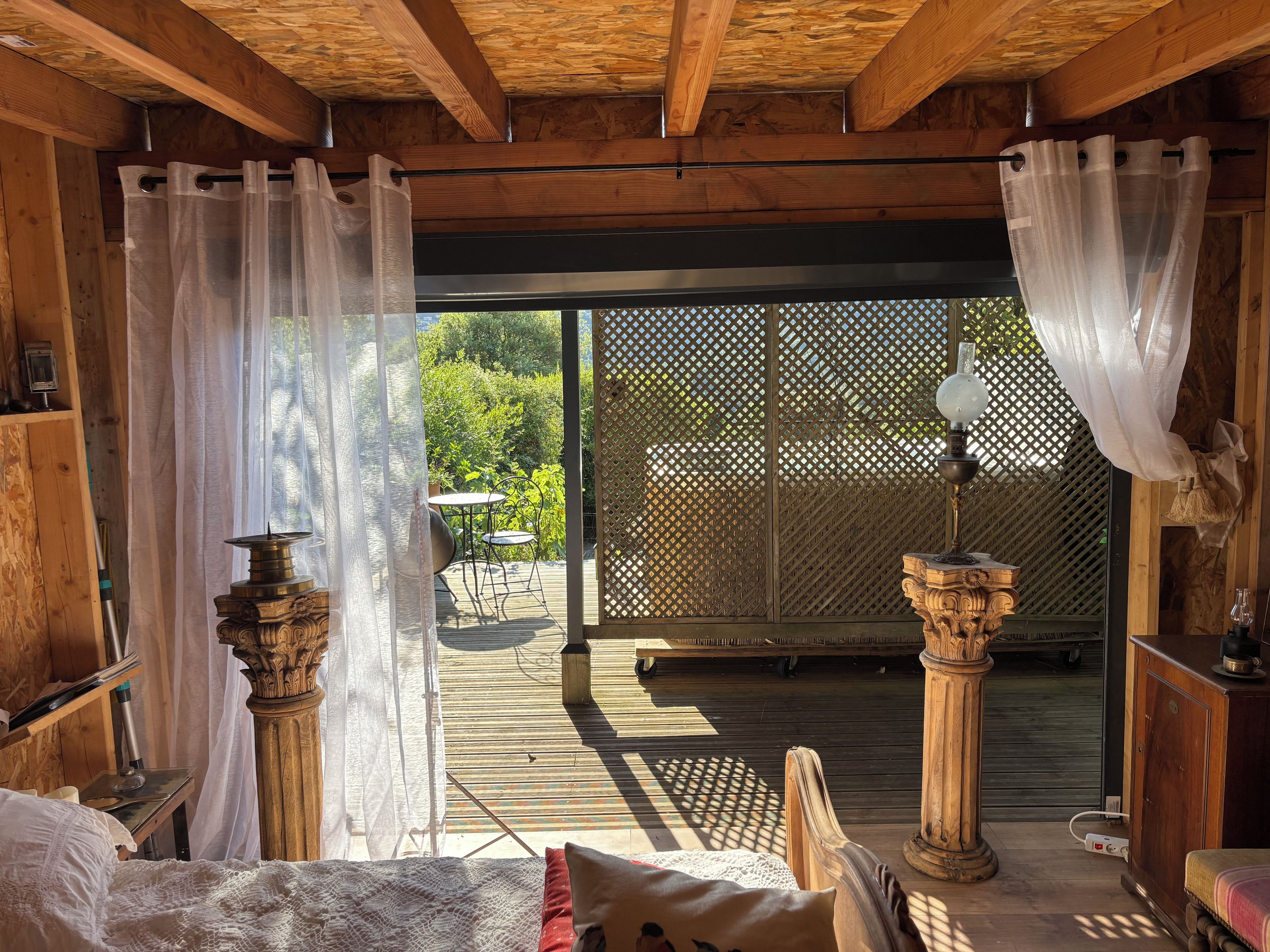 Um quarto de madeira com uma cama, uma mesa com abajur e vista para um deck externo por uma porta de madeira.