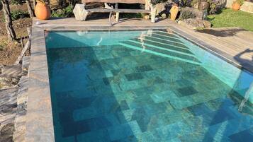 A rectangular swimming pool with clear water, surrounded by a stone deck and wooden benches.