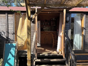 A wooden cabin with a kitchen area, a dining table, and a staircase leading to the entrance.