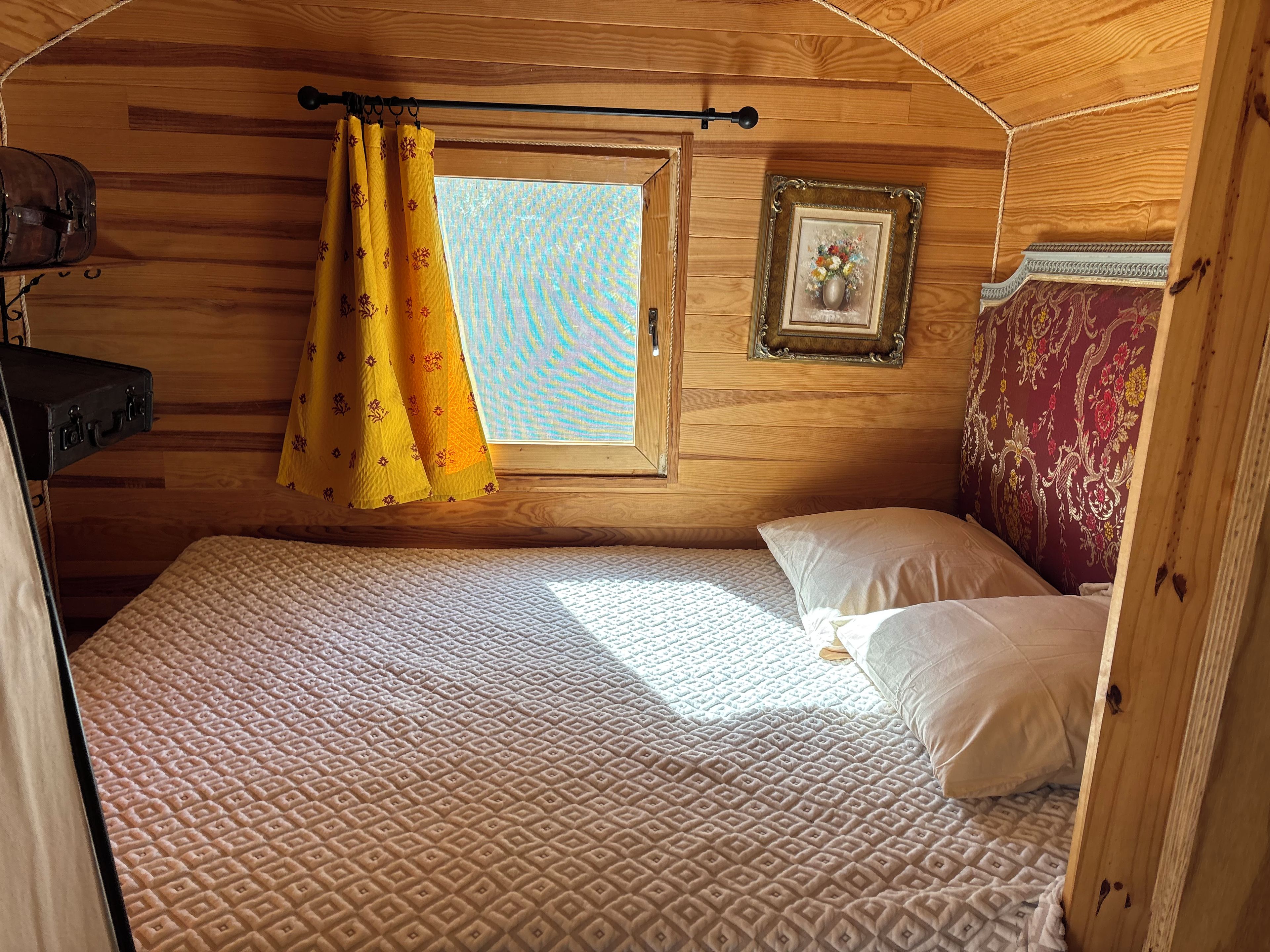 Une pièce confortable avec un lit, une fenêtre avec des rideaux, un cadre photo et une valise.