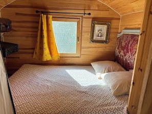 A cozy room with a bed, a window with curtains, a picture frame, and a suitcase. - Charming Travel Trailer – A Unique, Peaceful Getaway (Carbuccia)