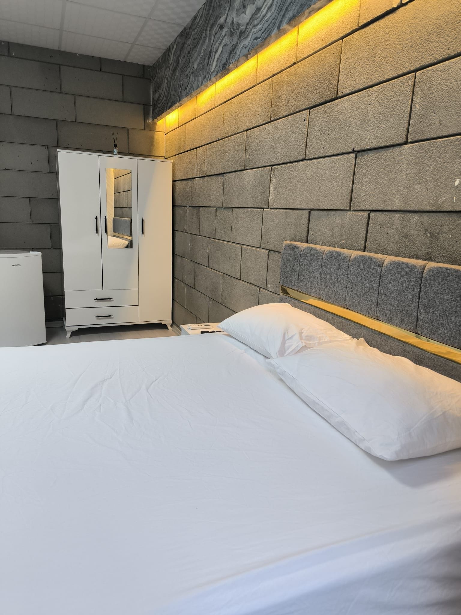 A bedroom with a bed, a wardrobe, and a headboard against a stone wall.