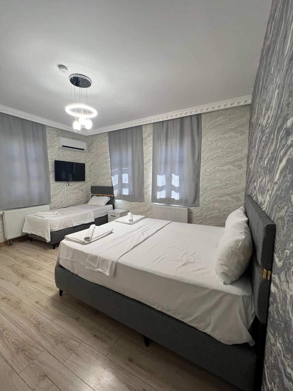 Habitación de hotel con una cama grande, otra más pequeña, un televisor de pantalla plana y una lámpara en el techo.