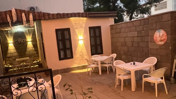 An outdoor patio with white plastic chairs and tables, a potted plant, and a brick wall. - SUR-U ALA HOTEL (Diyarbakır)