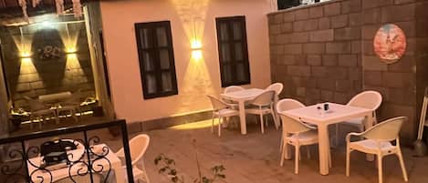 Un patio al aire libre con sillas y mesas de plástico blanco, una planta en maceta y un muro de ladrillo.