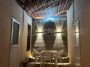 Un patio con mesa y sillas, techo con diseño y luces fijadas a la pared.