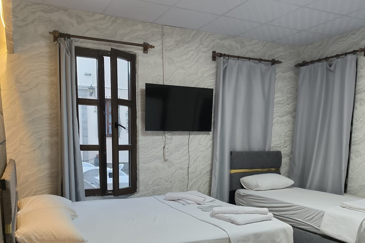Habitación de hotel con dos camas, un televisor y una ventana con cortinas.