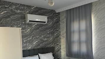 Quarto moderno com cama, paredes cinzentas, janela com cortinas e ar condicionado.