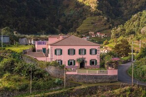 Eine pinkfarbene Villa mit Ziegeldach, umgeben von üppigem Grün und einer Steinmauer.