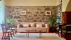 Una sala de estar con pared de piedra, un sofá color beige, sillas de madera, una mesa de centro y una araña.