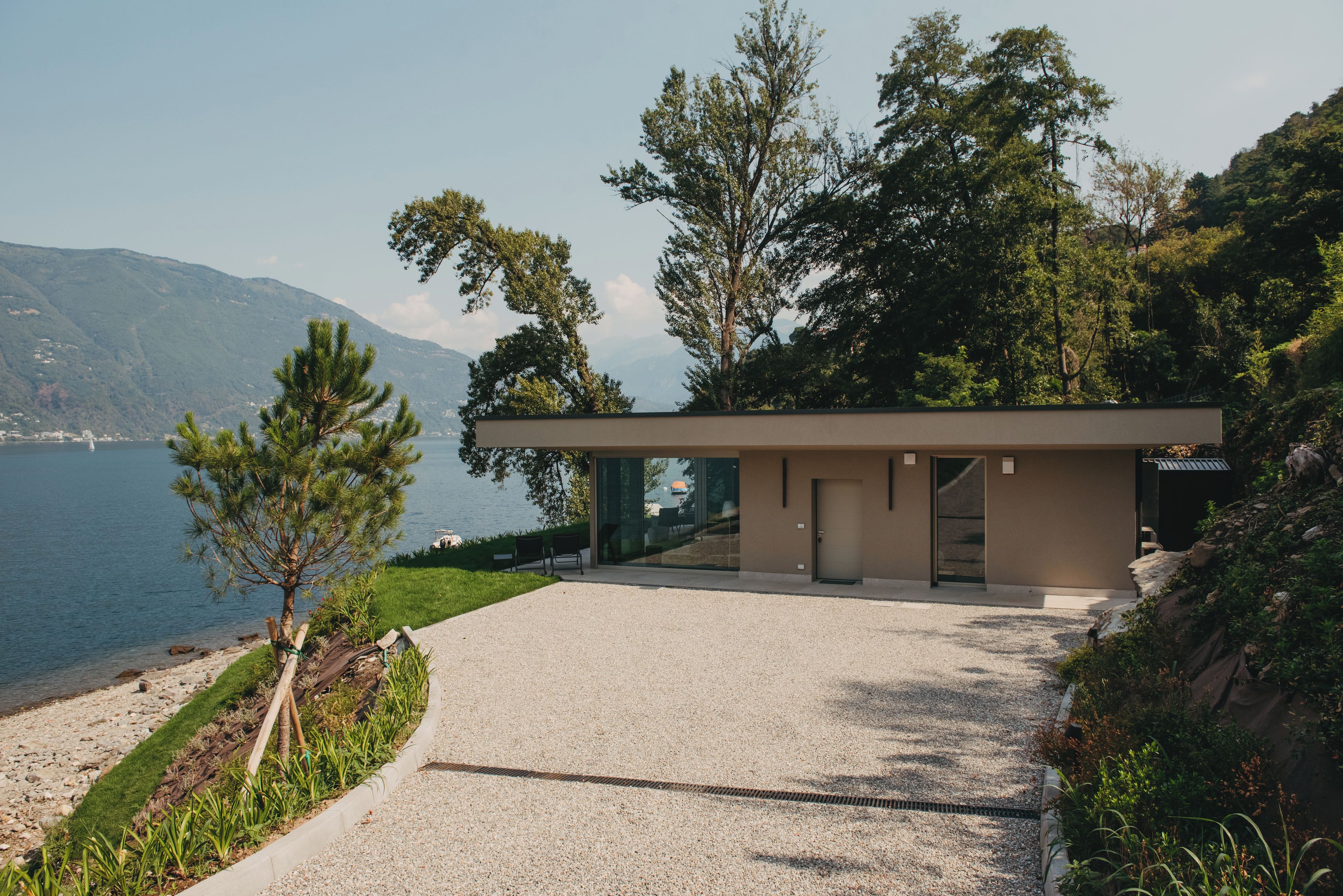 Un bâtiment moderne avec une allée en gravier, une entrée avec une porte en verre et une vue sur la mer et les montagnes.