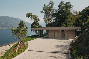 A modern building with a gravel driveway, a glass door entrance, and a view of the sea and mountains. - Villa Piccola Anna (Luino)