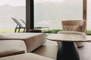 A modern living room with a view of mountains, a sofa, a chair, and a small table. - Villa Piccola Anna (Luino)