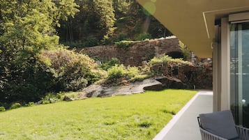 Un espacio exterior moderno con un muro de piedra, abundante vegetación y una vista despejada de una cadena montañosa.