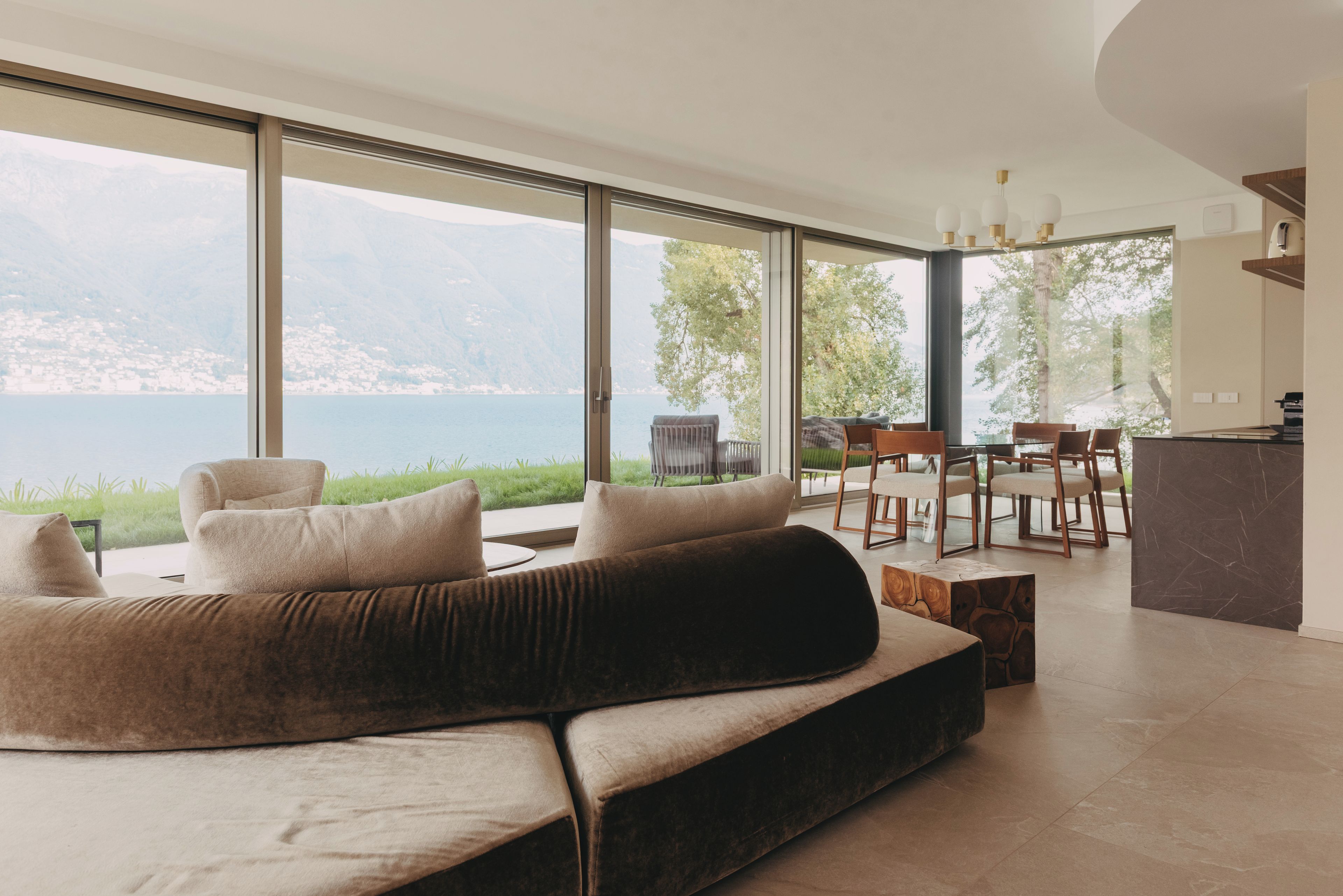 A modern living room with a large sofa, dining area, and a view of a lake.