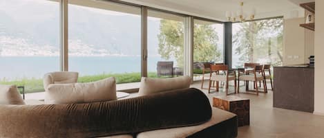 A modern living room with a large sofa, dining area, and a view of a lake.