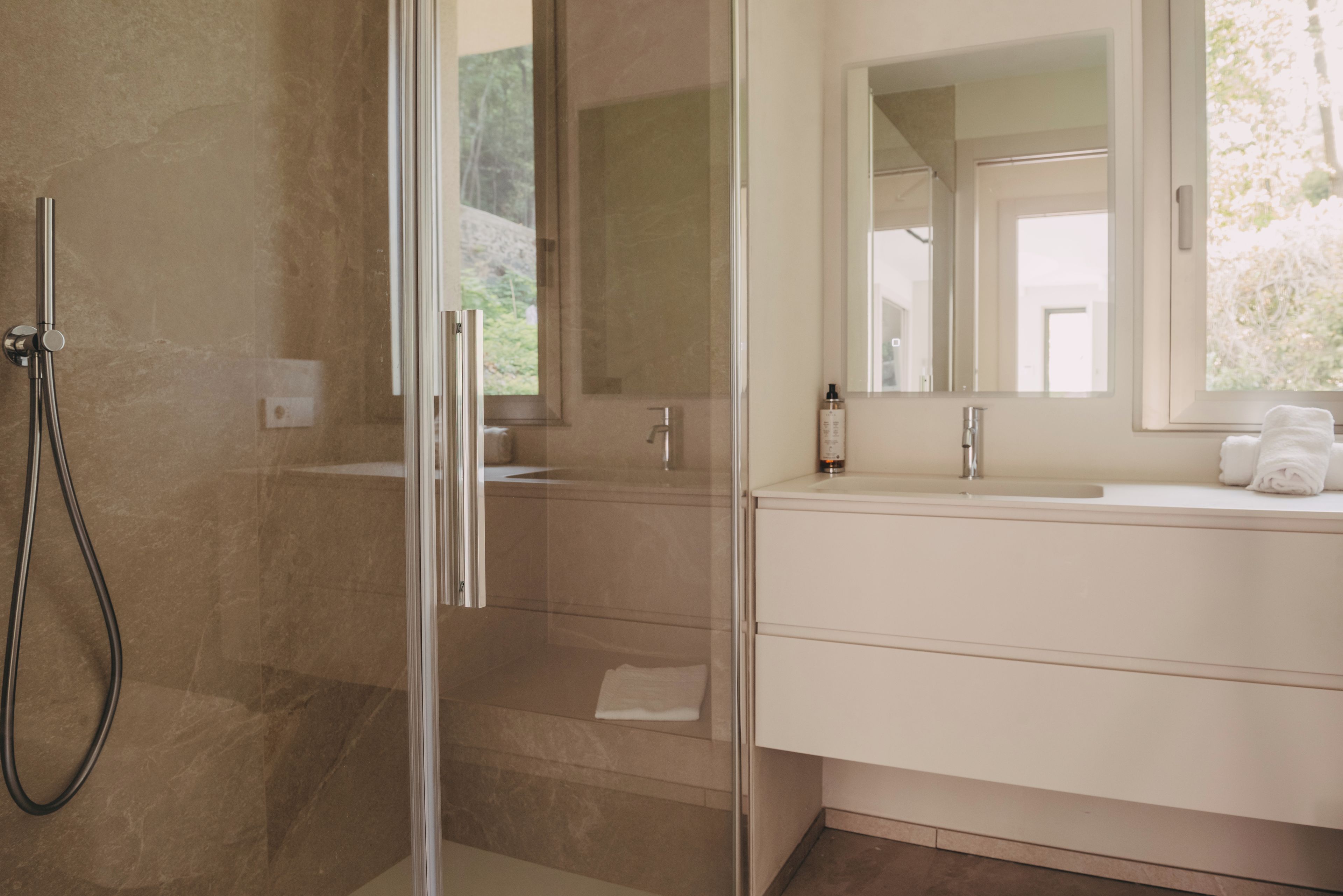 A modern bathroom with a glass shower enclosure, a white vanity with a mirror, and a window providing natural light.