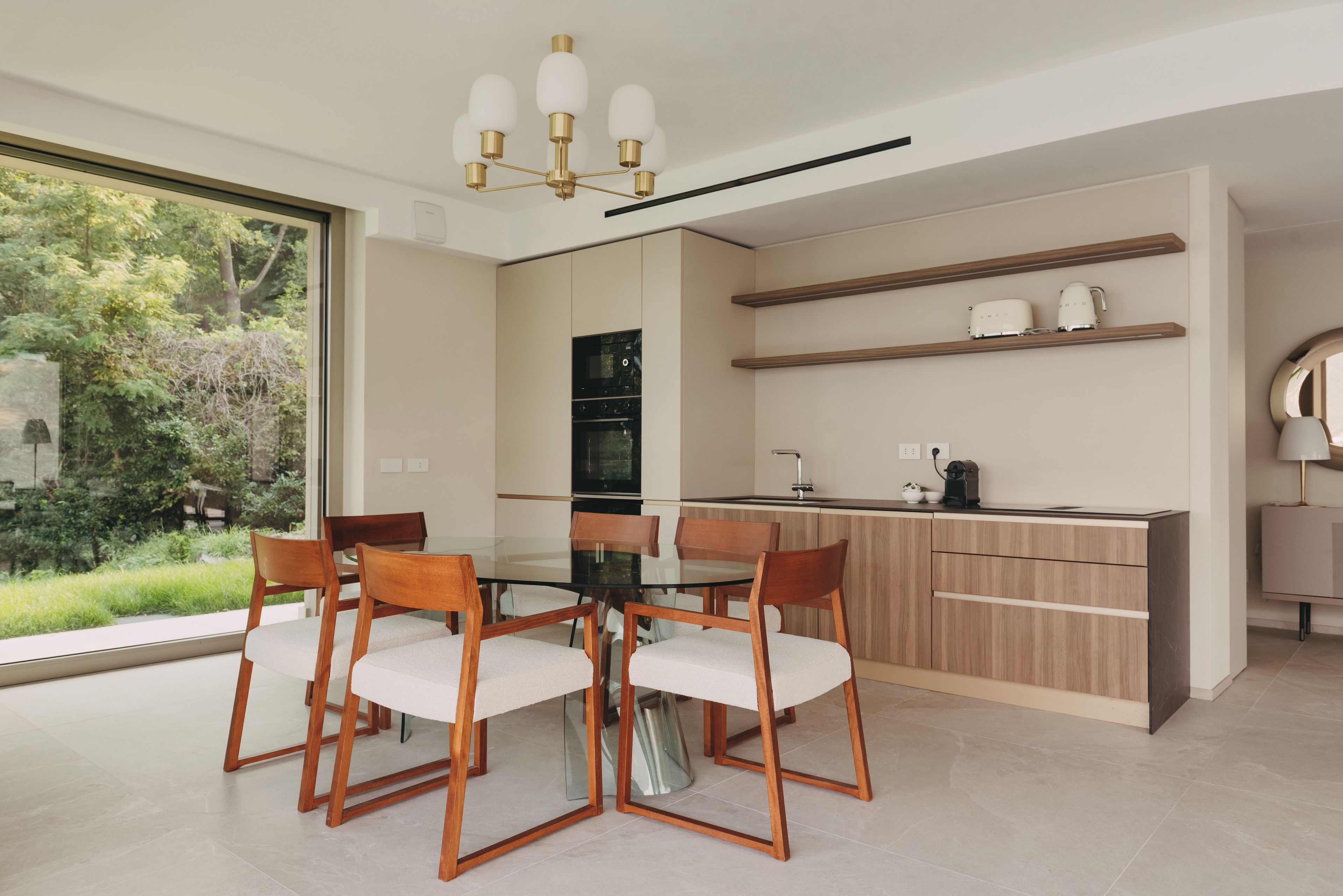 Une cuisine moderne avec un coin repas, comprenant une table en verre, des chaises en bois et un four encastré.