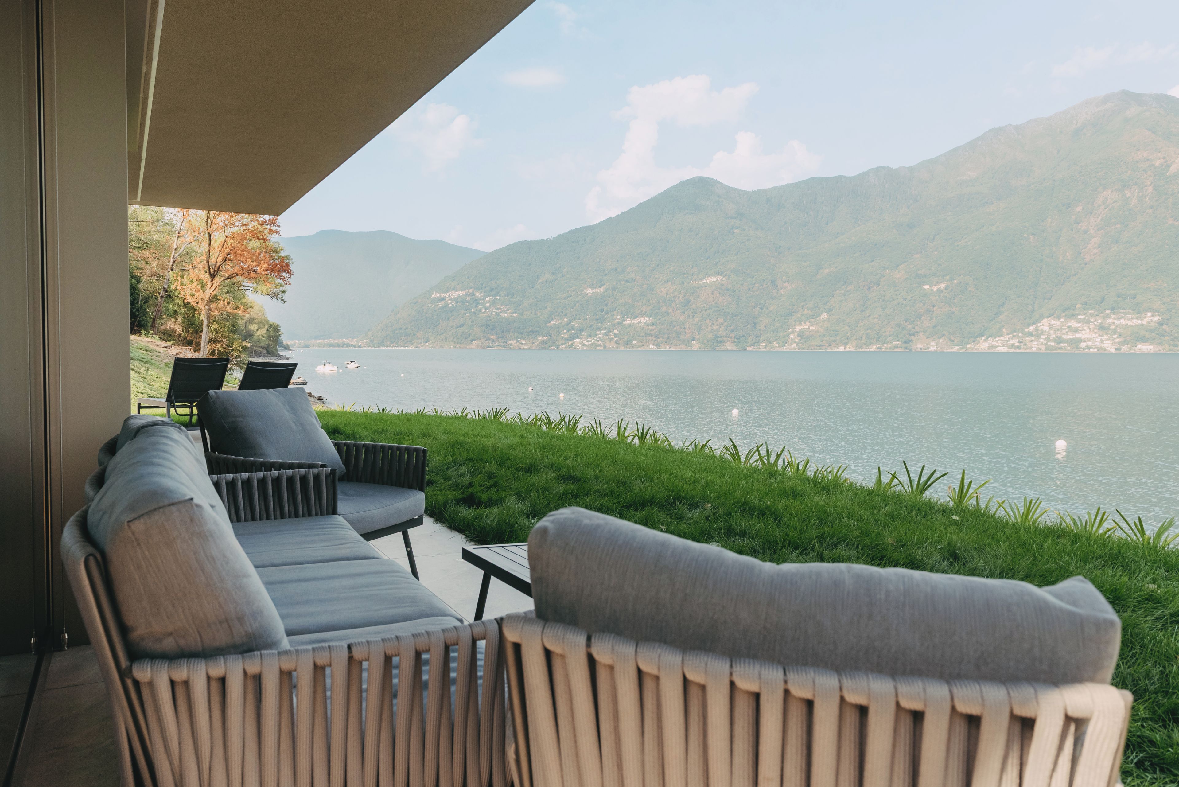 A balcony with a sofa and chairs overlooking a lake and mountains.