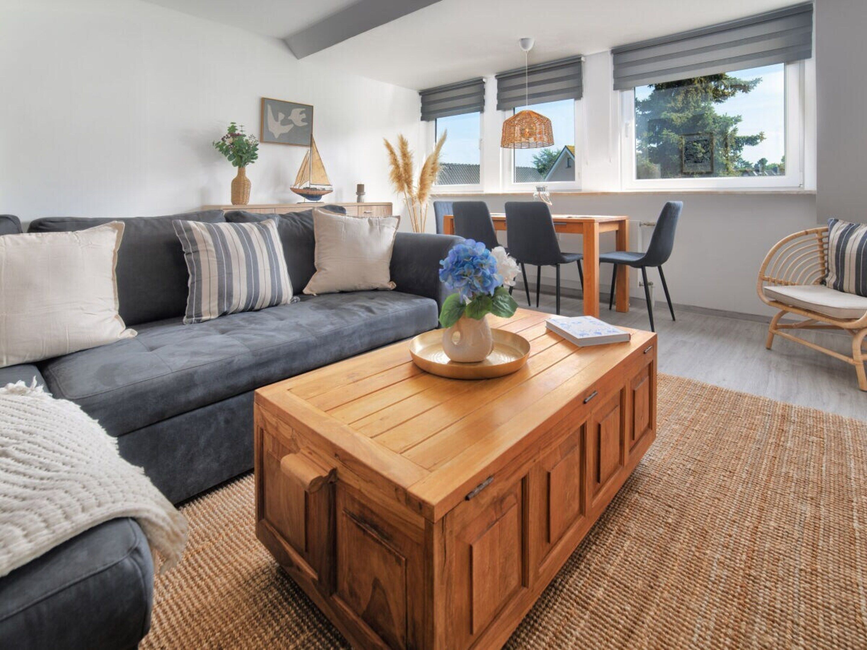 A modern living room with a grey sofa, wooden coffee table, and a dining area with a table and chairs.