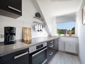A modern kitchen with a coffee maker, wooden cutting board, hanging utensils, and a window with a view. - Holiday Apartment With 2 Bedrooms (Heiligenhafen)