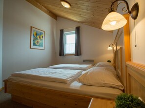 Ein Zimmer mit zwei Holzbetten, einem mit Vorhängen versehenen Fenster, einer Wandleuchte und einem gerahmten Bild.
