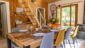 Un coin repas avec une table en bois, dressée pour quatre personnes et entourée de chaises, situé dans une cabane aux murs en bois et dotée d’un escalier.