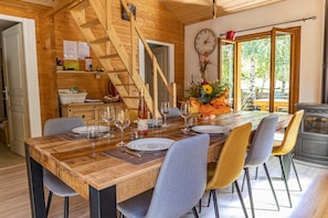A dining area with a wooden table set for four, surrounded by chairs, in a cabin with wooden walls and a staircase.