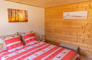 A bedroom with a wooden wall, a bed with red and white bedding, and two paintings. - Chalet 'Des Sources, Avec Spa' with Mountain View, Private Terrace and Wi-Fi (Ramonchamp)