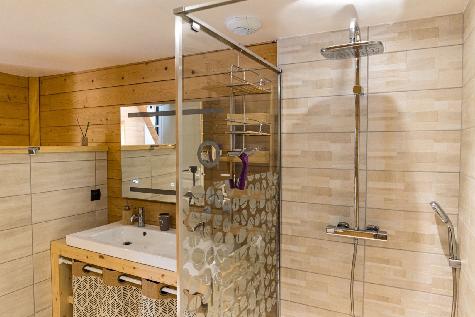 A modern bathroom with a glass-enclosed shower, a wooden vanity, and a mirror.
