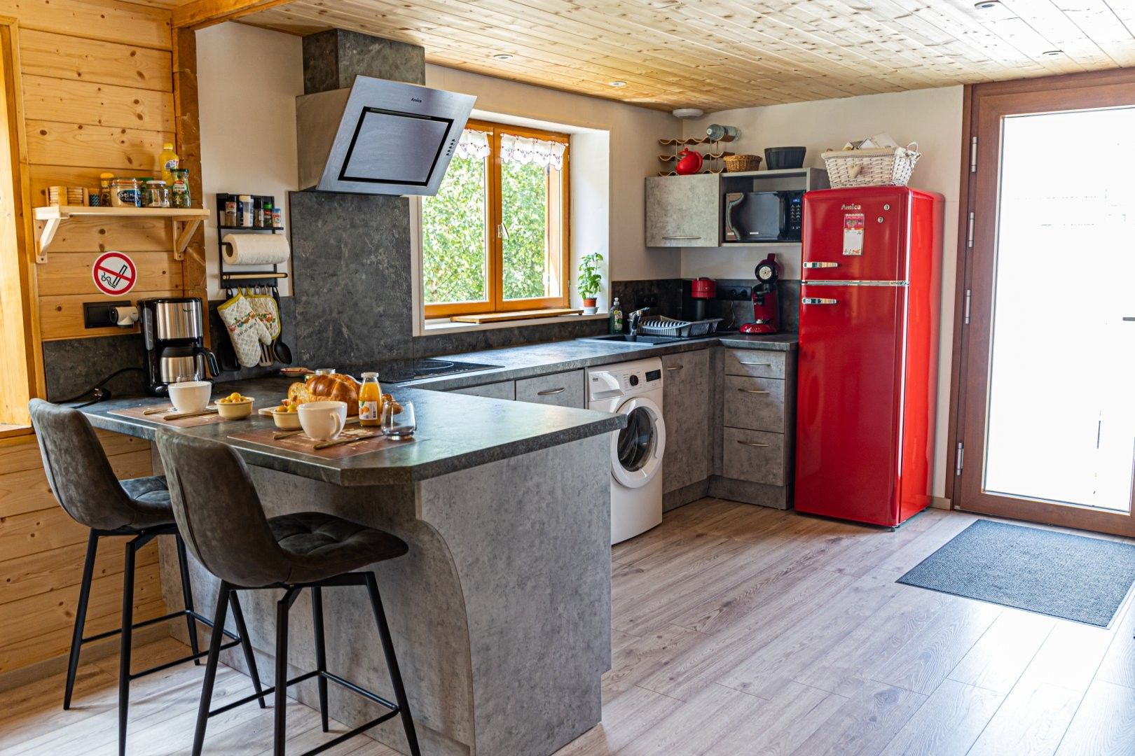 Cozinha moderna com máquina de lavar embutida, geladeira vermelha e uma janela grande.