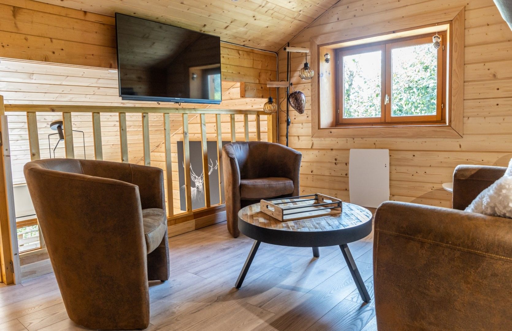 A cozy cabin interior with a TV mounted on the wall, wooden flooring, and a round table with chairs.
