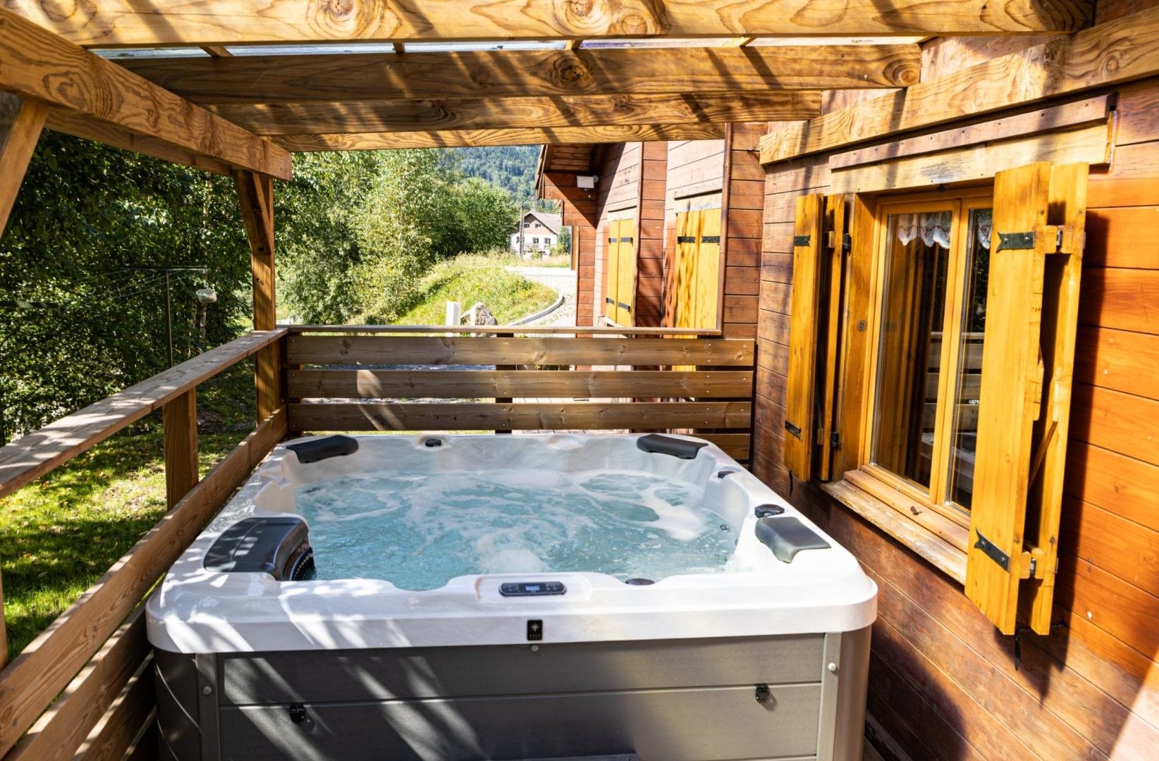 En træterrasse med jacuzzi, trægelændere og et hus i baggrunden.