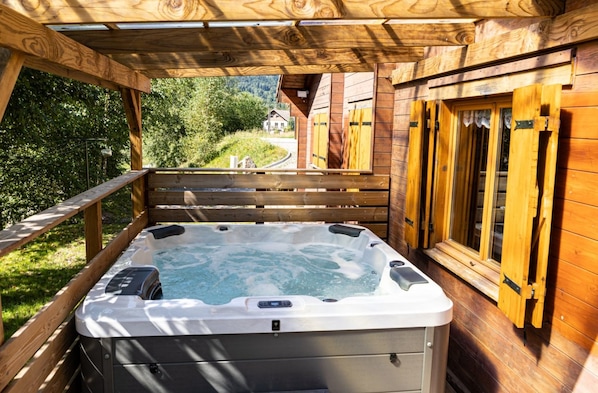 A wooden deck with a hot tub, wooden railings, and a view of a house in the background.