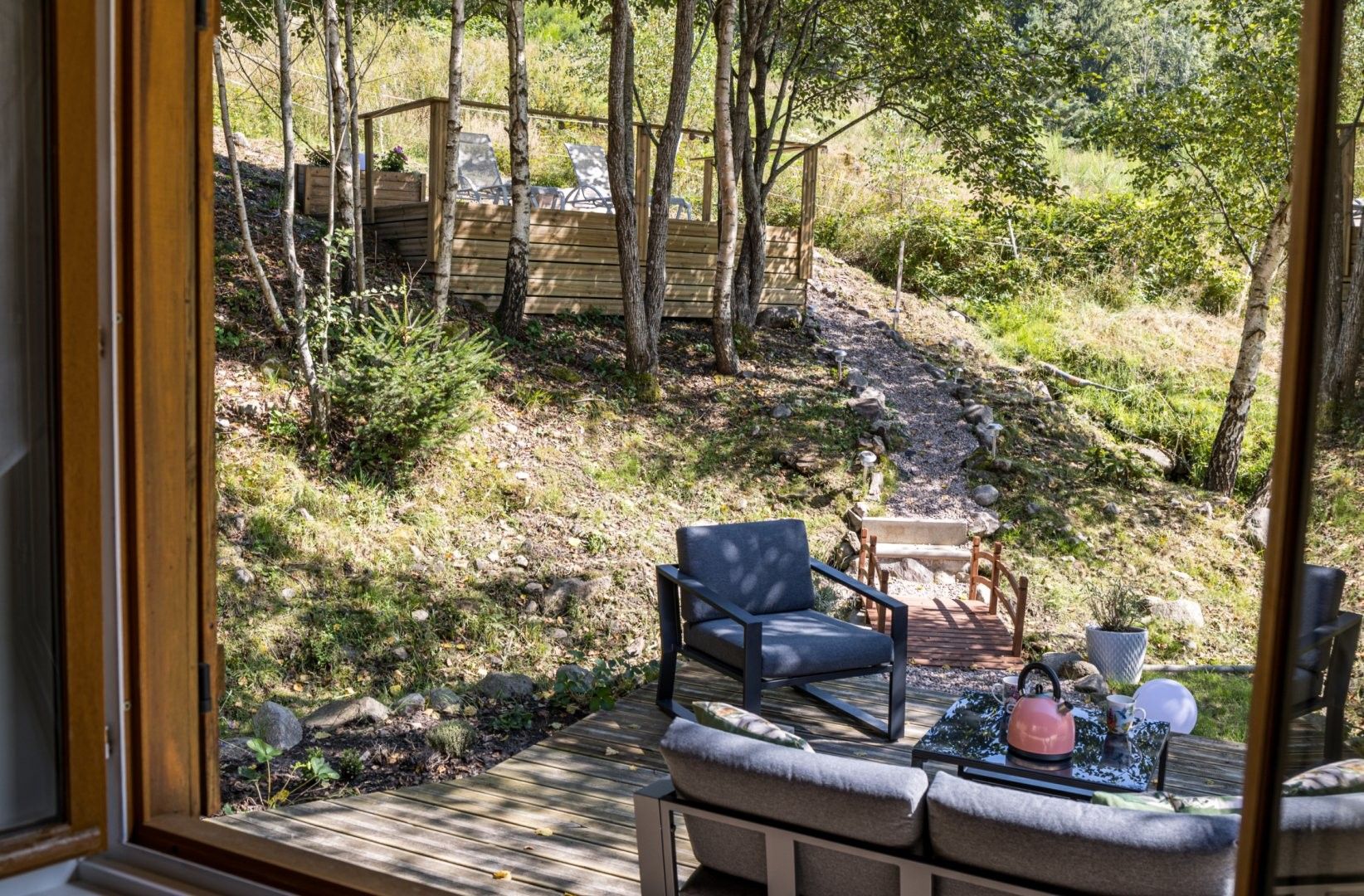 Eine Terrasse mit Gartenmöbeln, Blick auf ein bewaldetes Gebiet und eine Holzhütte im Hintergrund.