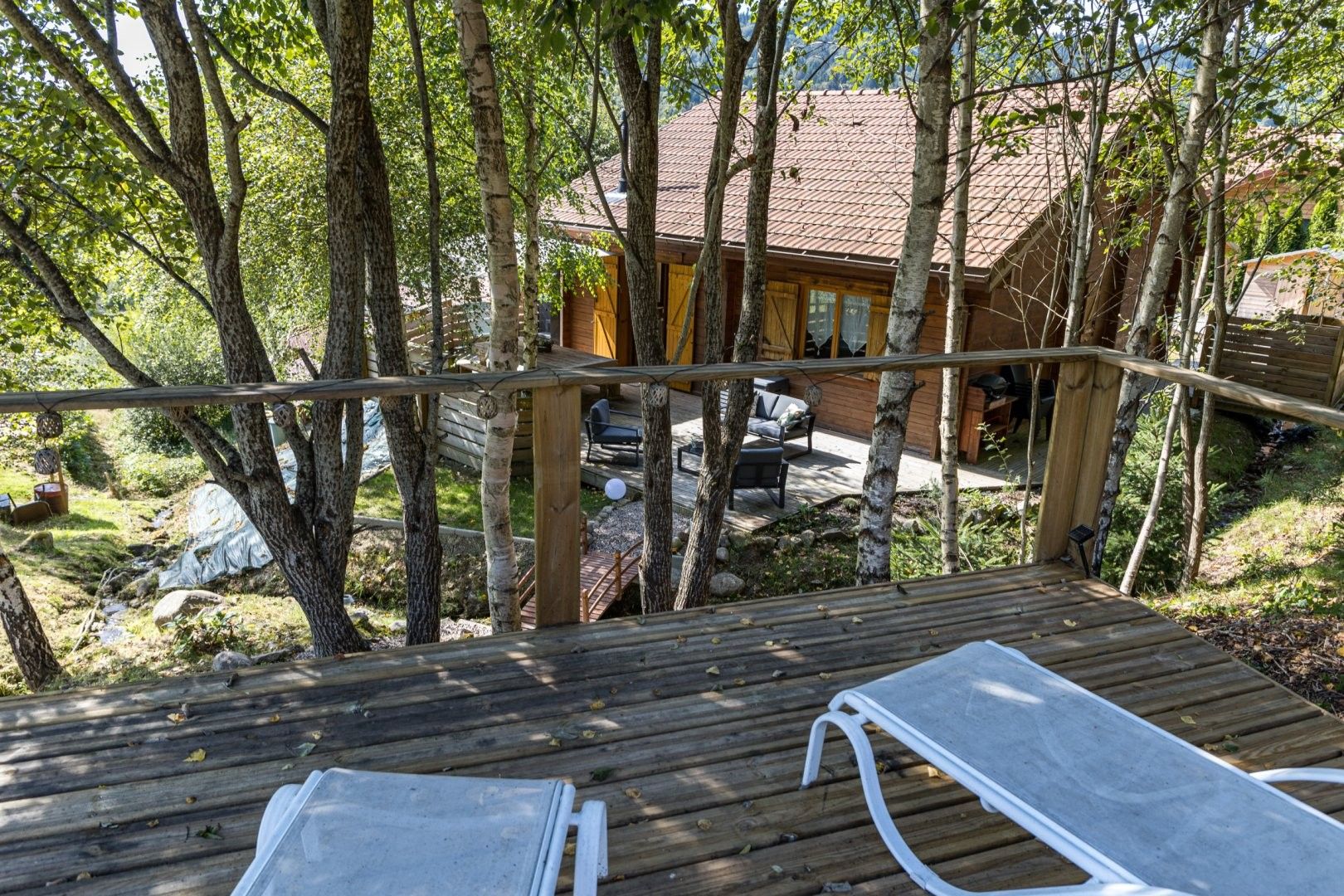A wooden deck with two lounge chairs, overlooking a cabin with a tiled roof and a patio area.