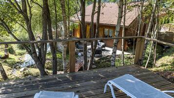 A wooden deck with two lounge chairs, overlooking a cabin with a tiled roof and a patio area.