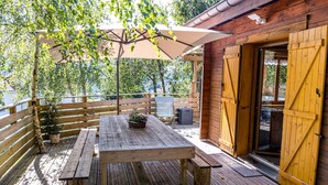 Une terrasse extérieure en bois, avec une table de pique-nique et des bancs, une clôture en bois et un bâtiment doté d’une porte en bois.